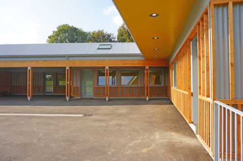 Extension et rénovation du groupe scolaire de Berville, par Atelier Cosme Architecture. Vue de la galerie-préau en bois depuis la cour.