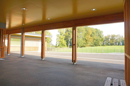 Extension et rénovation de l'école de Berville, par Atelier Cosme Architecture. Vue sur le clos-masure depuis la galerie-préau en bois.