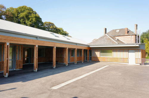 Extension et rénovation de l'école de Berville, par Atelier Cosme Architecture. Vue de la galerie-préau en bois depuis la cour.