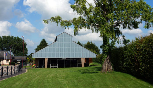 Garage et city-stade d'Alvimare par Atelier Cosme Architecture. Structure bois, façade bois, et volumes créent un masque contre la route départementale.